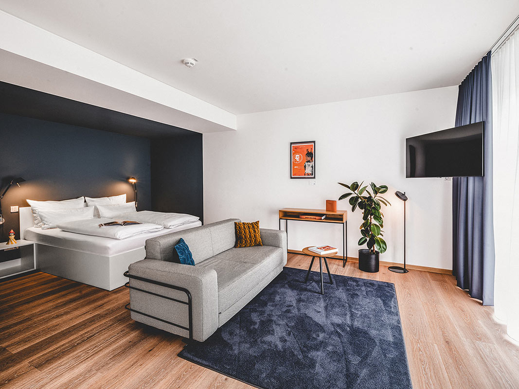 Stilvoll eingerichtete Sitzecke mit modernem Sofa und skandinavischen Möbeln und einem großen Doppelbett im Hintergrund in einer Unterkunft in Herzogenaurach.