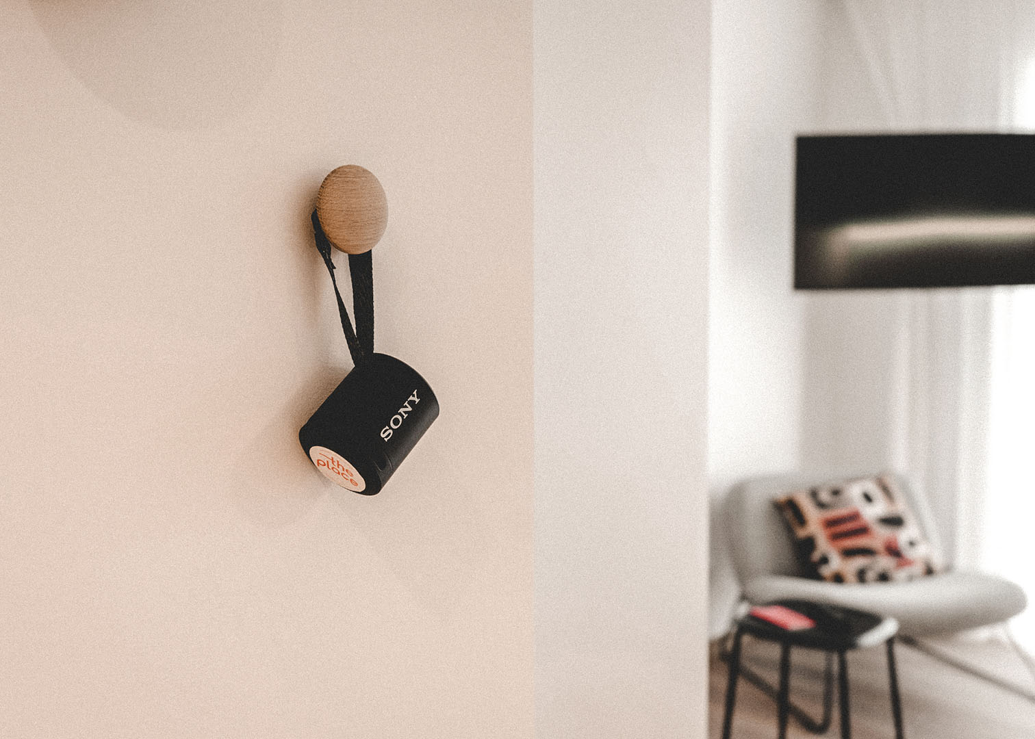 Tragbarer Sony-Lautsprecher an einem Holzhaken an der Wand, im Hintergrund unscharf ein Sessel mit gemustertem Kissen und Wandbildschirm