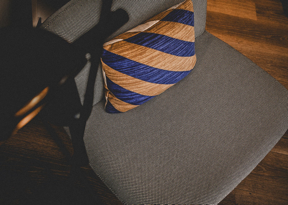Stuhl mit grauem Stoffbezug und Kissen mit diagonalen blauen und braunen Streifen auf Holzboden