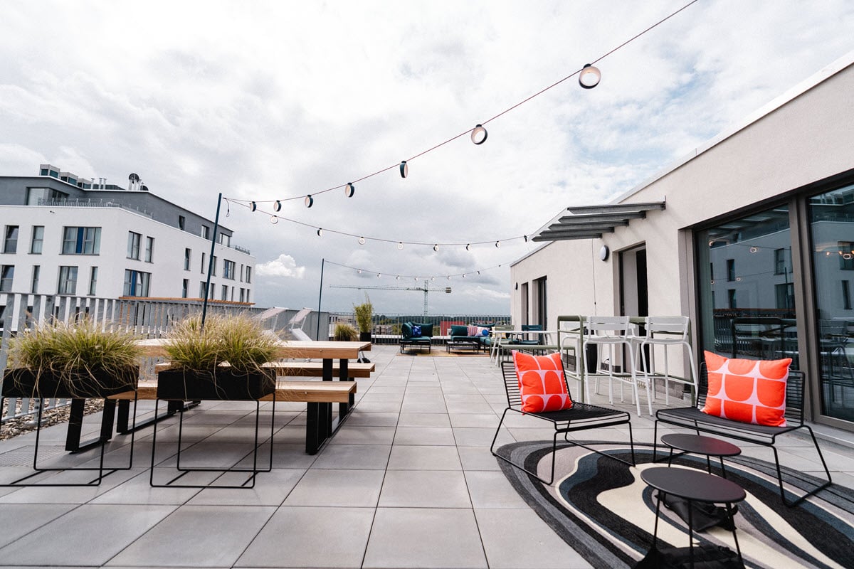 Dachterrasse mit Holzbänken, Lichterketten und farbenfrohen Sitzkissen