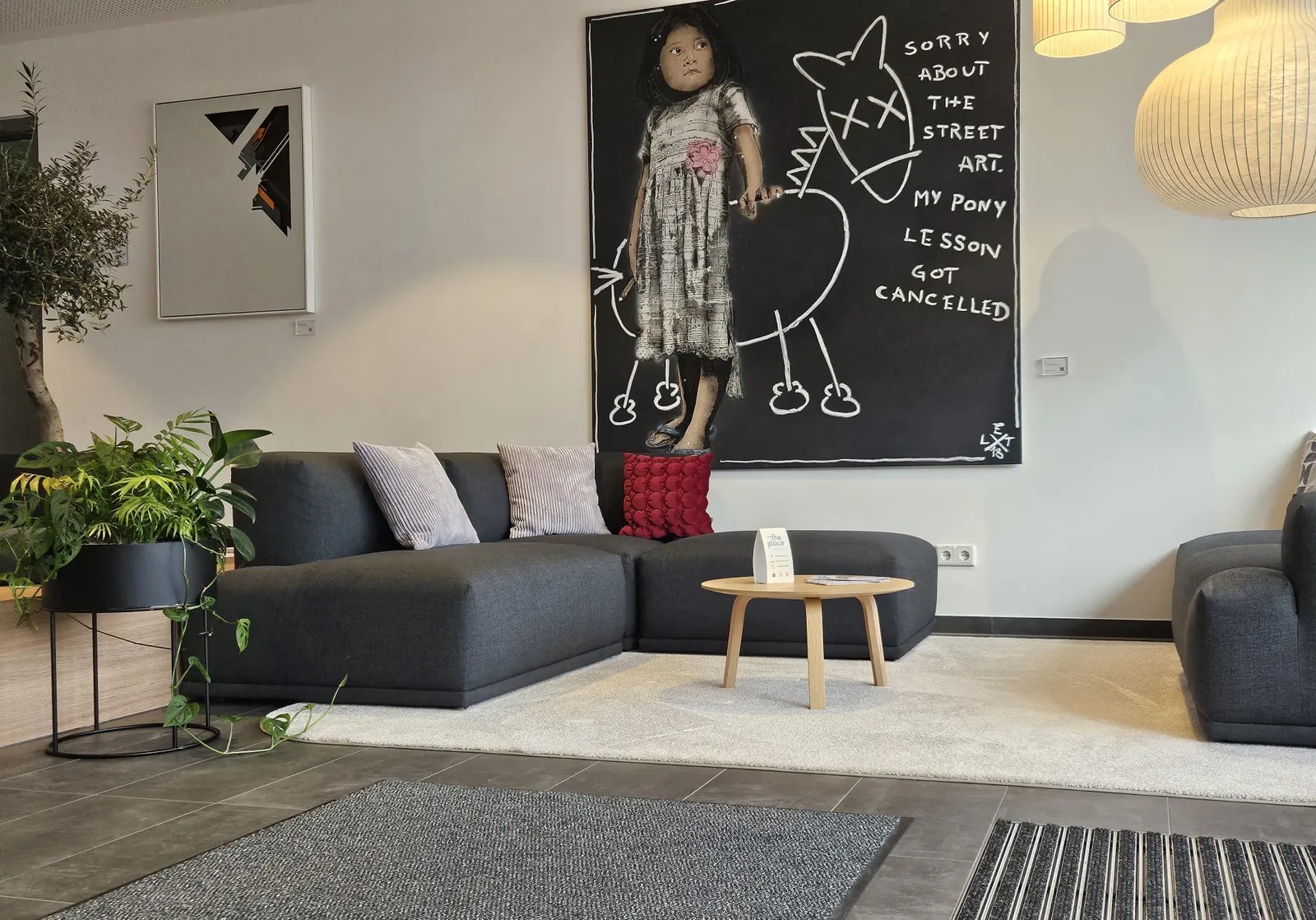 Lounge-Bereich mit dunkler Sofalandschaft, künstlerischem Wandbild und Holztisch